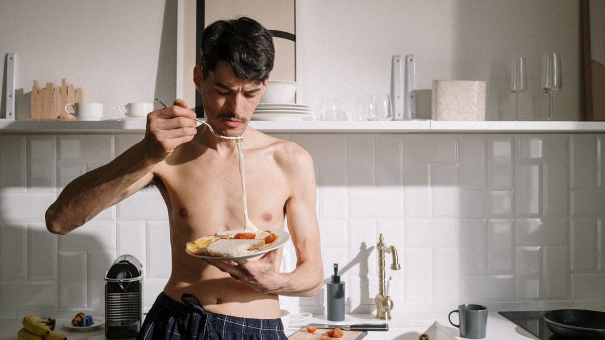 Young man enjoying a breakfast omelette in a sunlit kitchen setting.